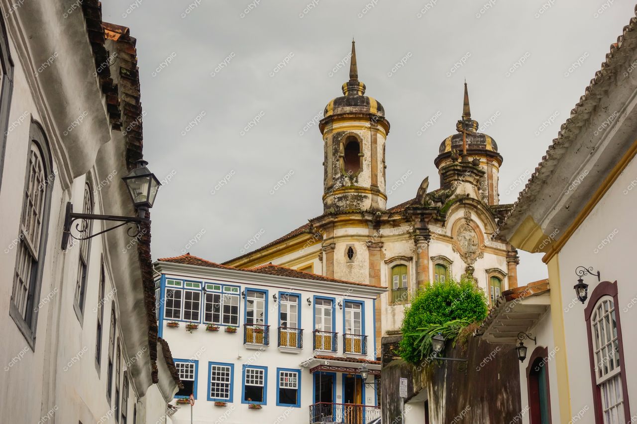 Ouro Preto, Minas Gerais, rua com arquitetura colonial e igreja ao fundo em dia nublado com vegetação ao redor