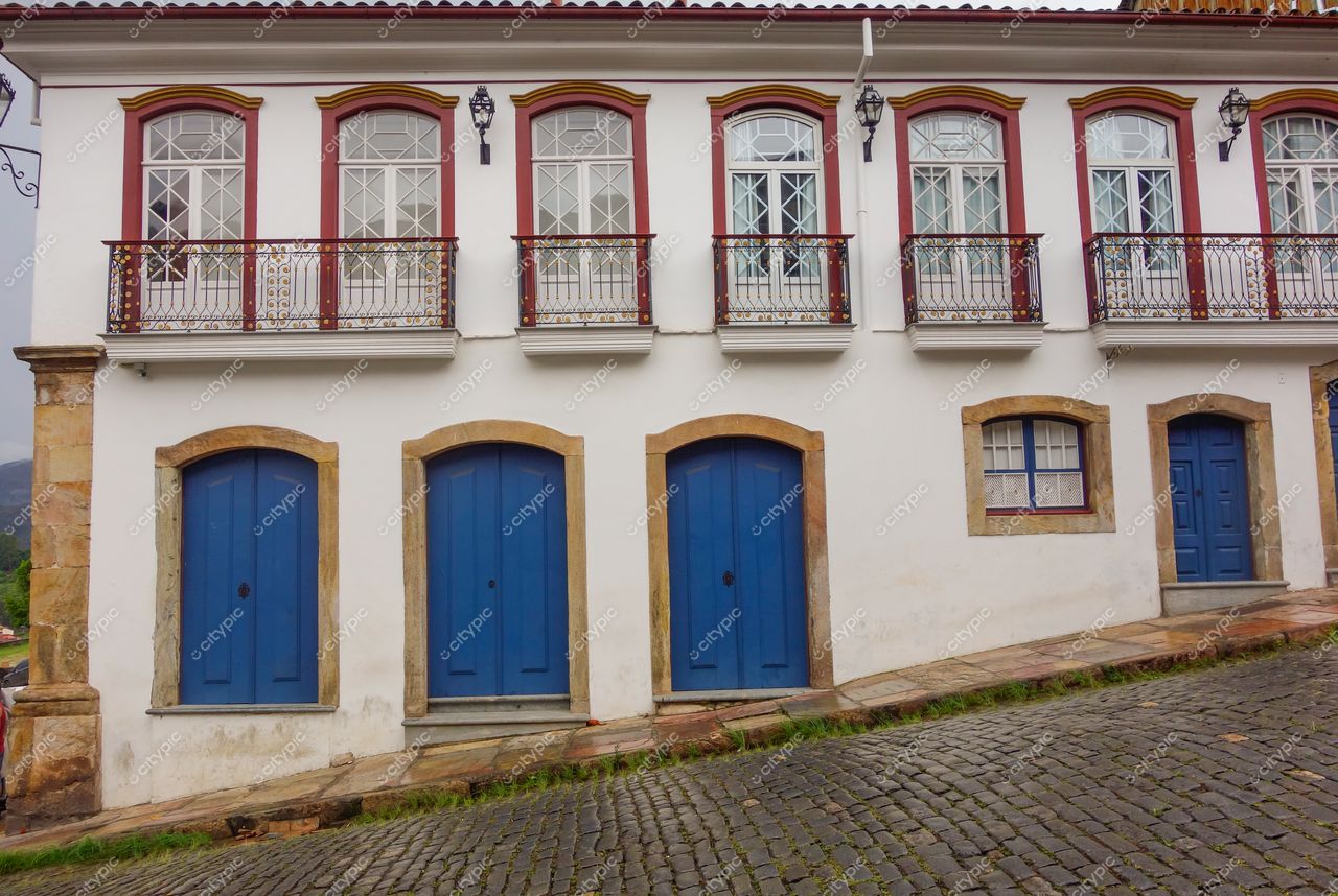 Ouro Preto, Minas Gerais, fachada colonial com janelas vermelhas e portas azuis em dia nublado e calçamento de paralelepípedos