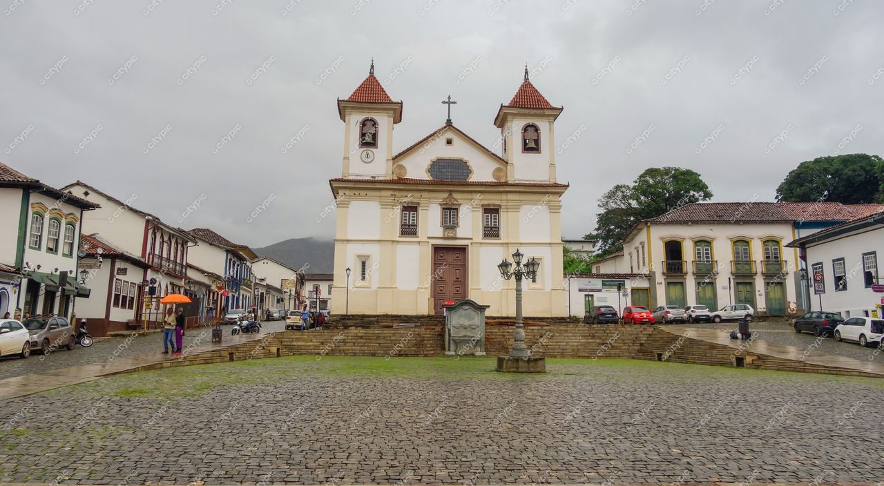 Praça Minas Gerais em Mariana com céu nublado, igreja branca e detalhes terrosos, ruas de pedras e tranquilidade