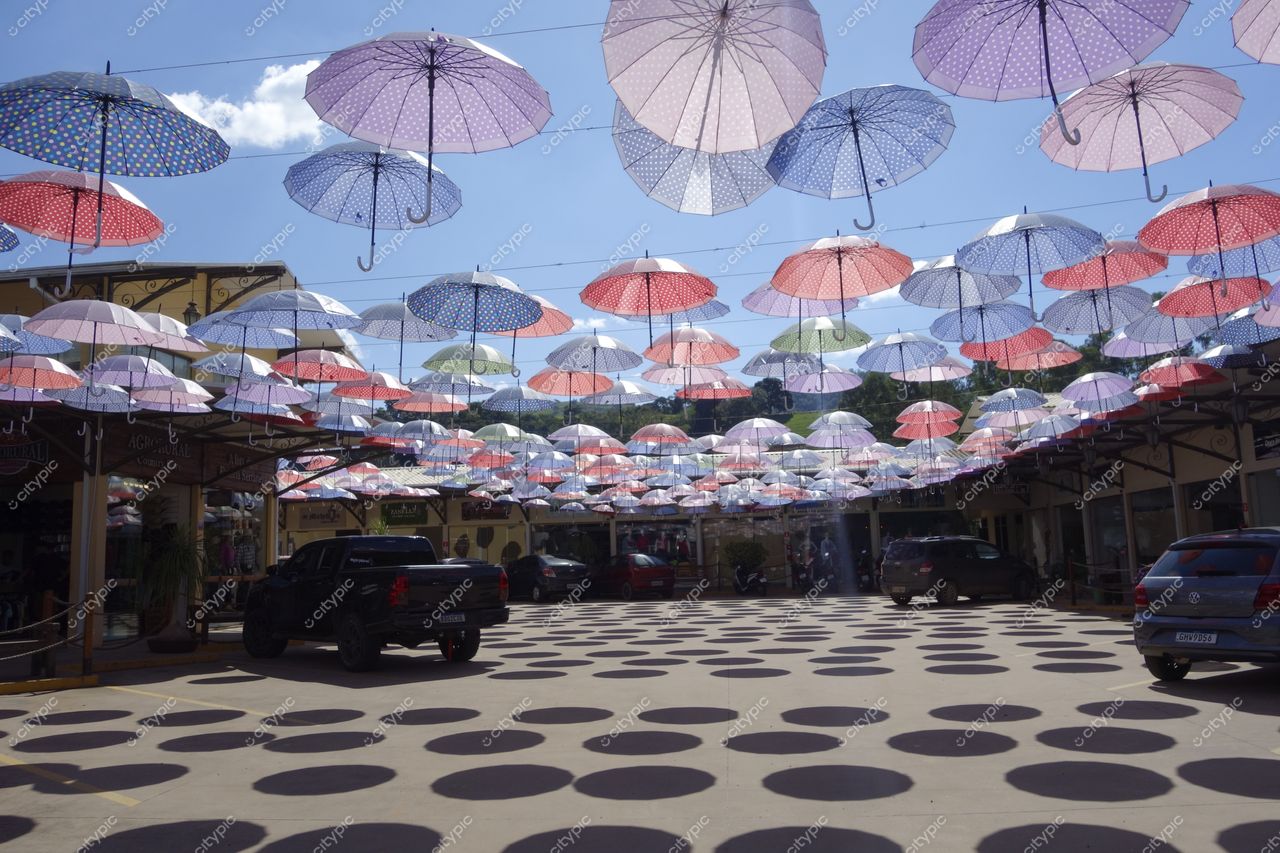 Socorro, São Paulo, praça ensolarada com guarda-chuvas coloridos pendurados e sombras circulares no chão