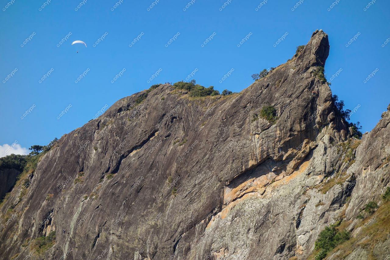 São Bento do Sapucaí, São Paulo, formação rochosa com vegetação esparsa e paraglider sob céu azul claro durante o dia