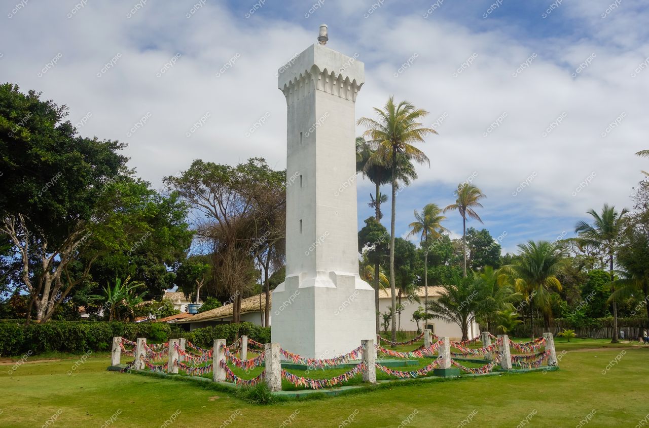 Centro Histórico de Porto Seguro em Porto Seguro com farol branco cercado por vegetação tropical e céu parcialmente nublado
