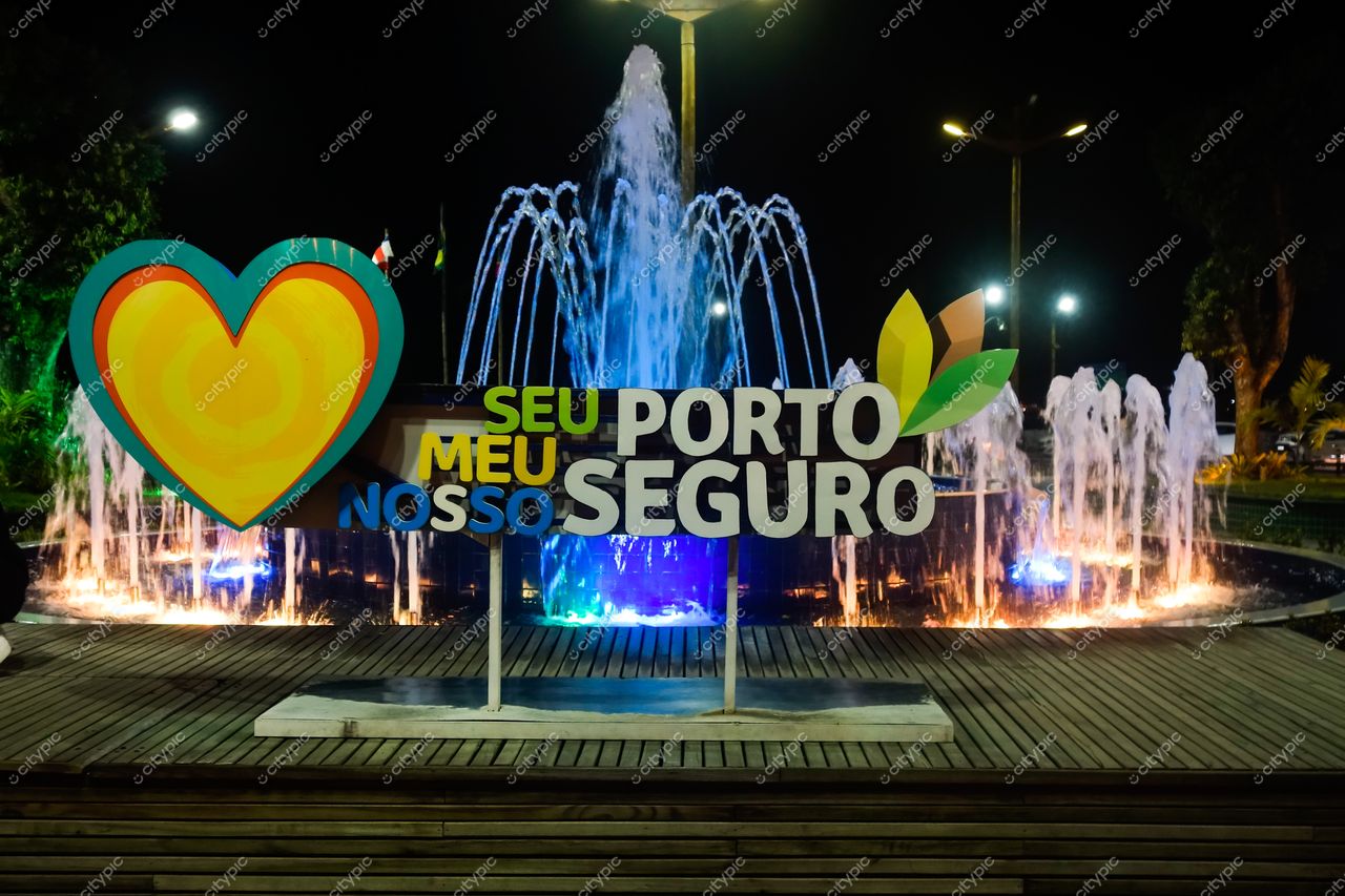 Passarela do Descobrimento em Porto Seguro com letreiro “Seu Porto Seguro” iluminado e fonte de água ao fundo à noite
