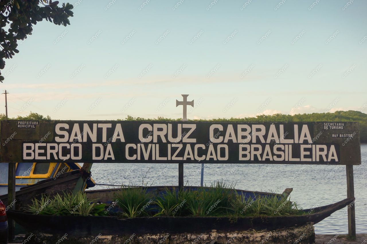 Berço da Civilização Brasileira em Santa Cruz Cabrália com placa em madeira, vegetação e embarcação ao fundo
