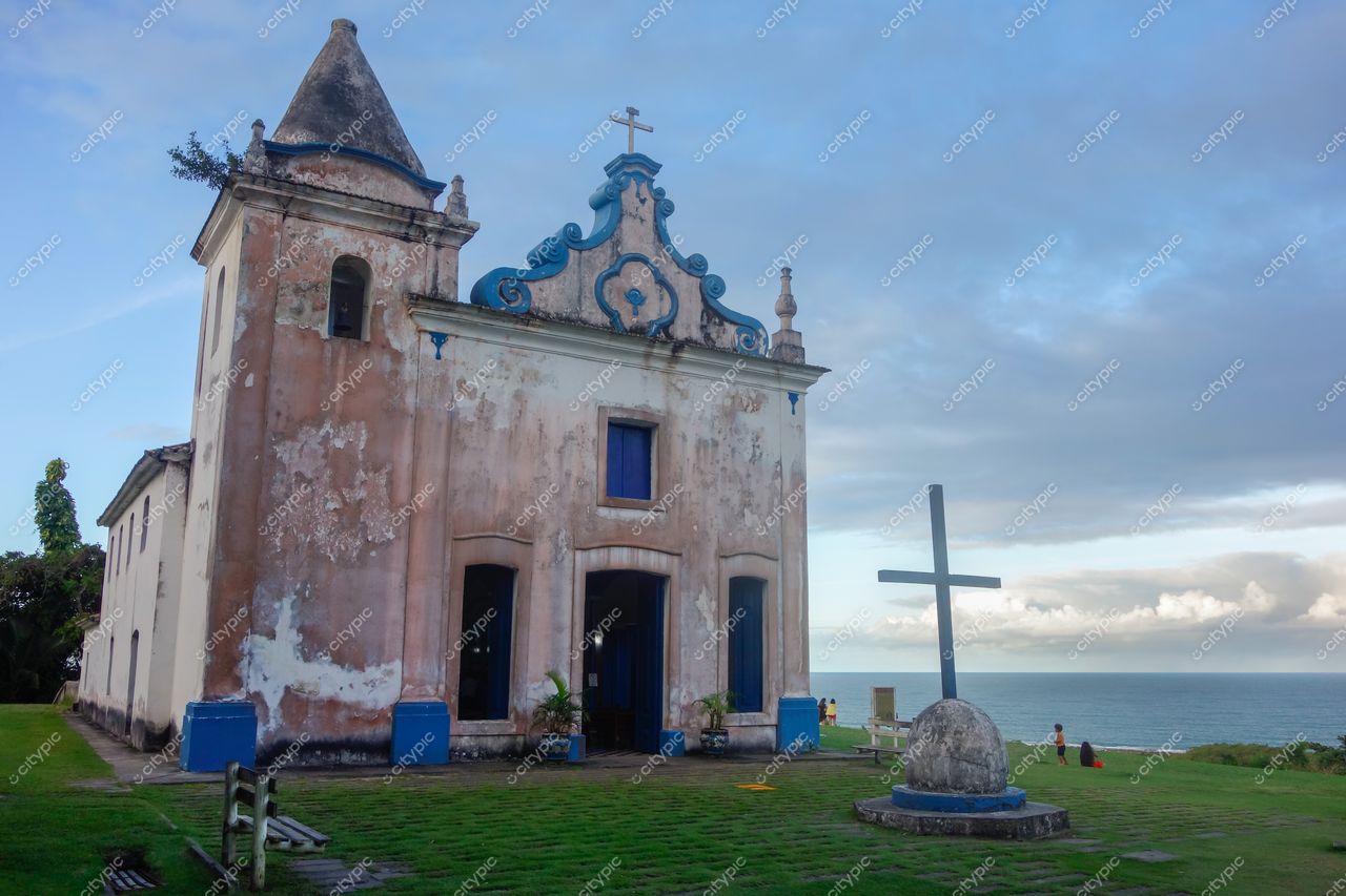 Igreja de Nossa Senhora da Conceição em Santa Cruz Cabrália com céu nublado e vegetação ao redor em manhã tranquila