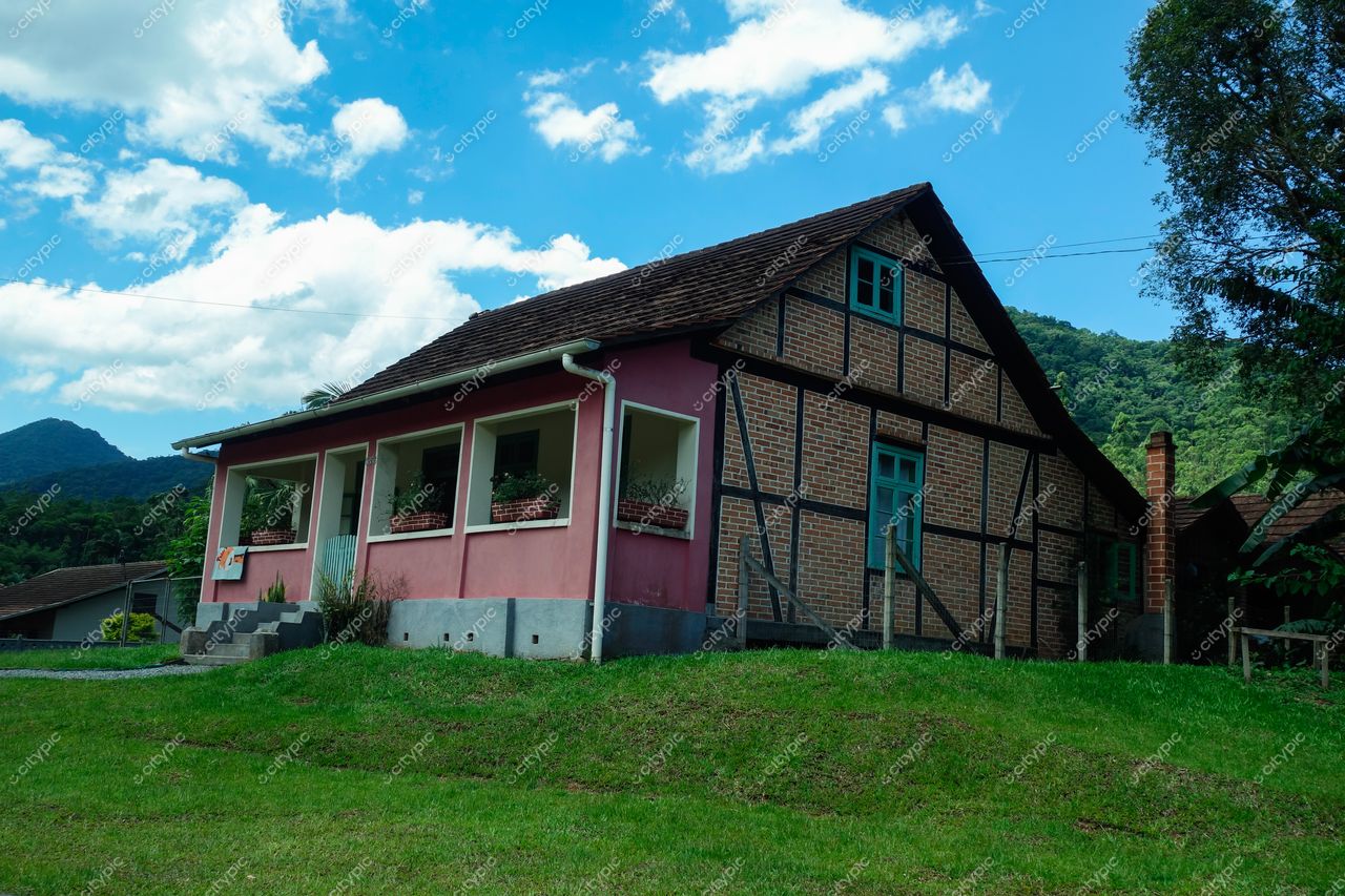 Pomerode, Santa Catarina, casa enxaimel rosa em paisagem verdejante com montanhas e céu azul ao fundo