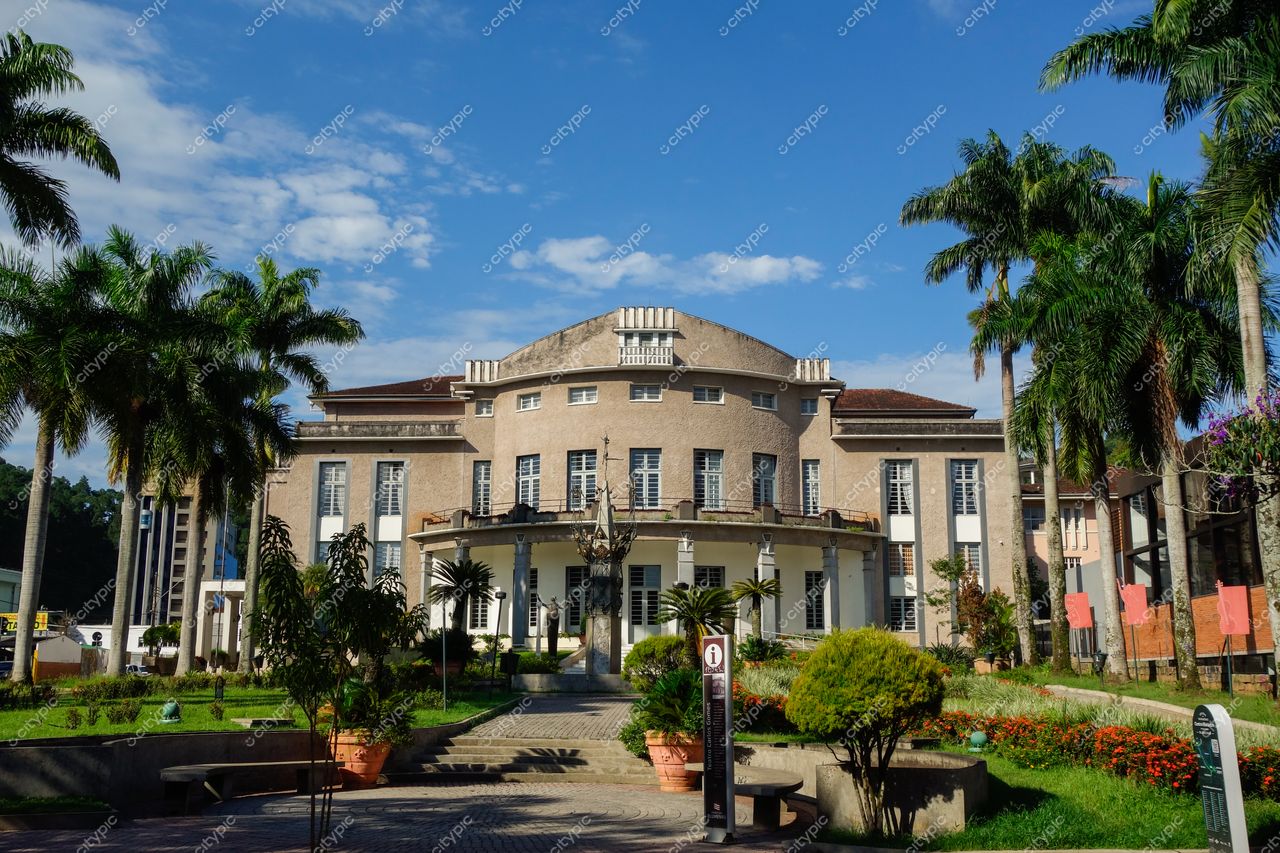 Blumenau, Santa Catarina, edifício de estilo marcante cercado por palmeiras e canteiros floridos em dia ensolarado