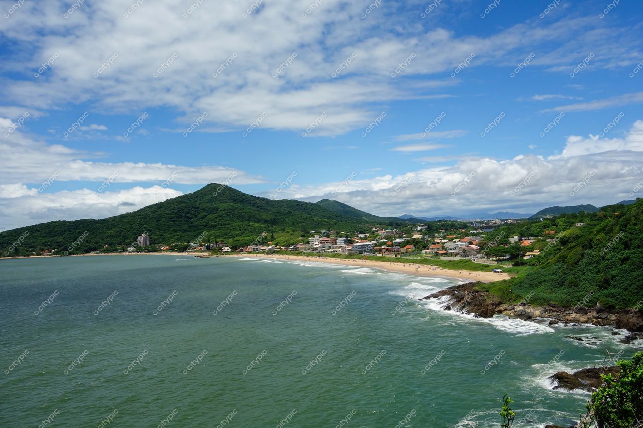 Penha, Santa Catarina vista panorâmica da praia com mar verde-esmeralda e colinas urbanas sob céu parcialmente nublado