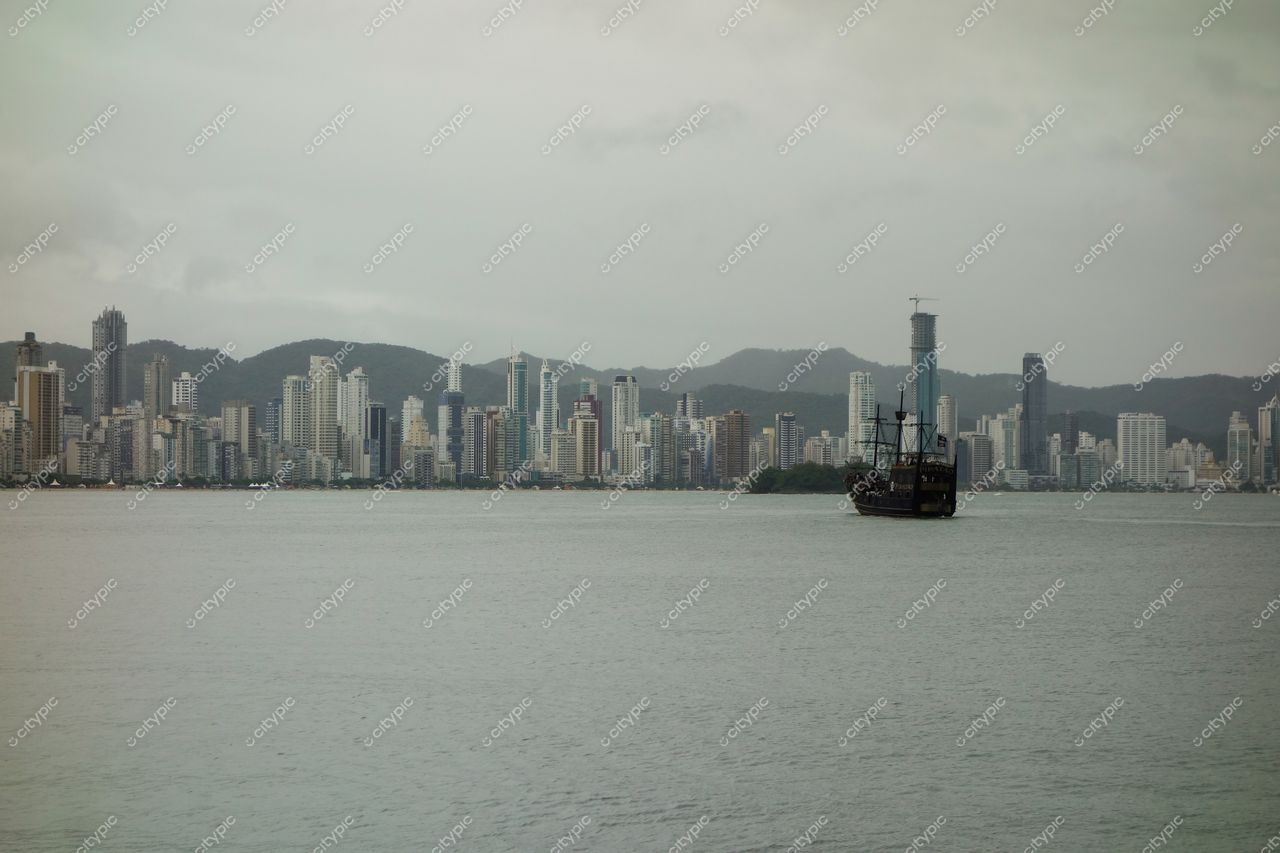 Balneário Camboriú, Santa Catarina, vista urbana com arranha-céus refletindo luz suave em dia nublado e barco antigo