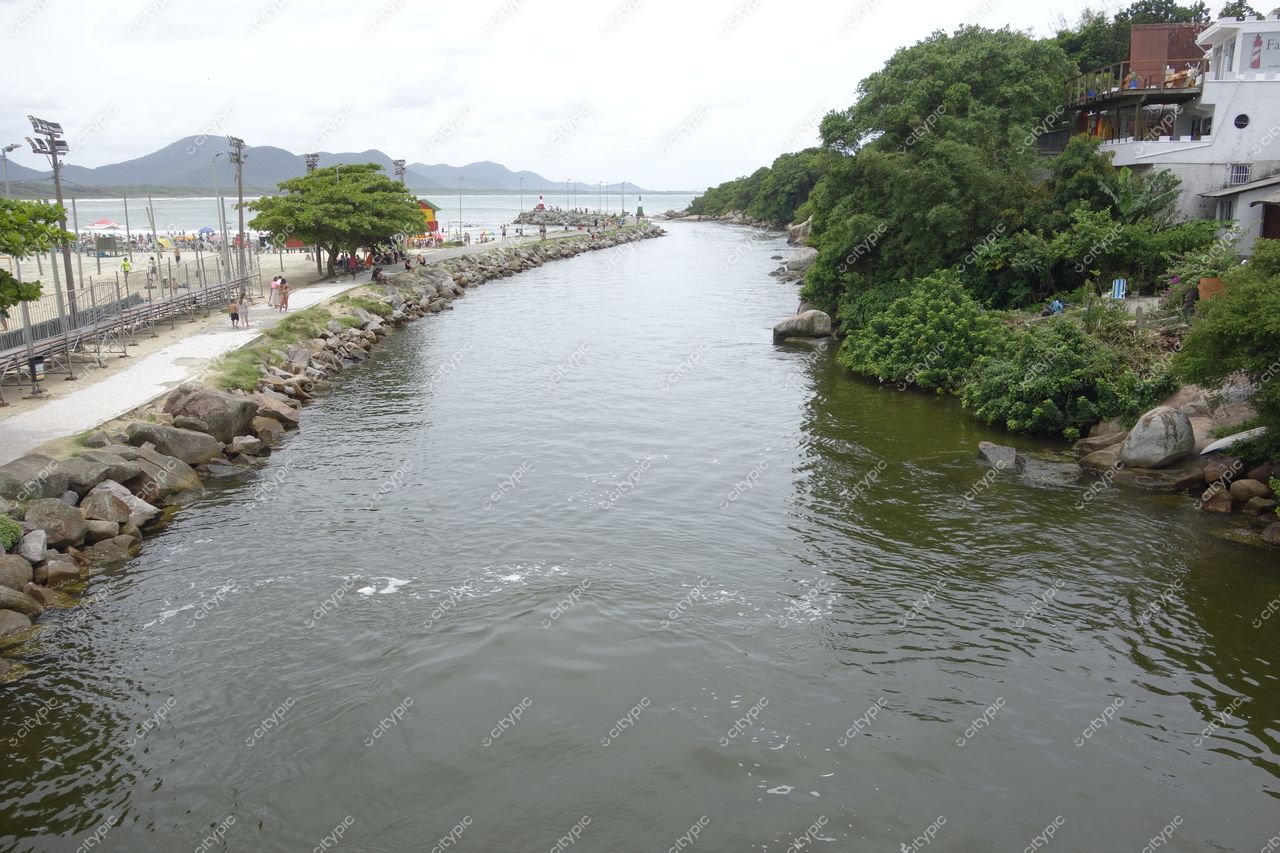 Florianópolis, Santa Catarina canal urbano com vegetação densa e pessoas caminhando sob céu nublado e luz difusa