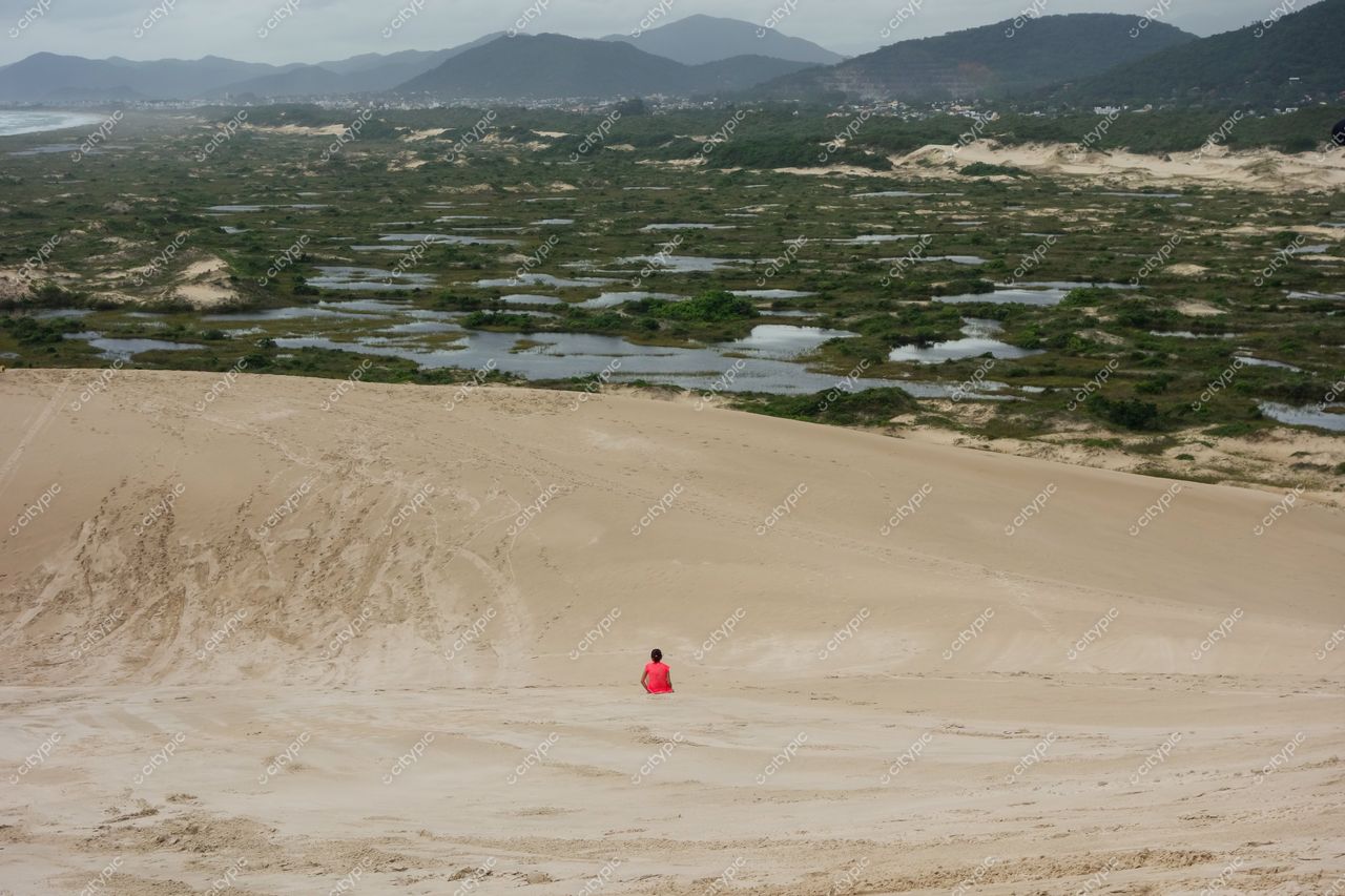 Florianópolis, Santa Catarina vista panorâmica de dunas com indivíduo em blusa rosa e céu nublado ao fundo