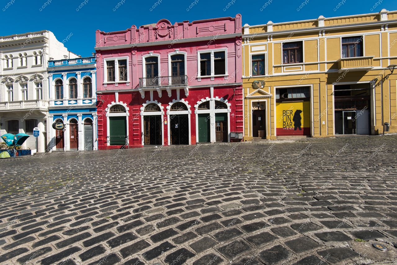 Curitiba, Paraná, centro histórico com edifícios coloridos e calçamento de paralelepípedos sob luz solar intensa e céu azul claro