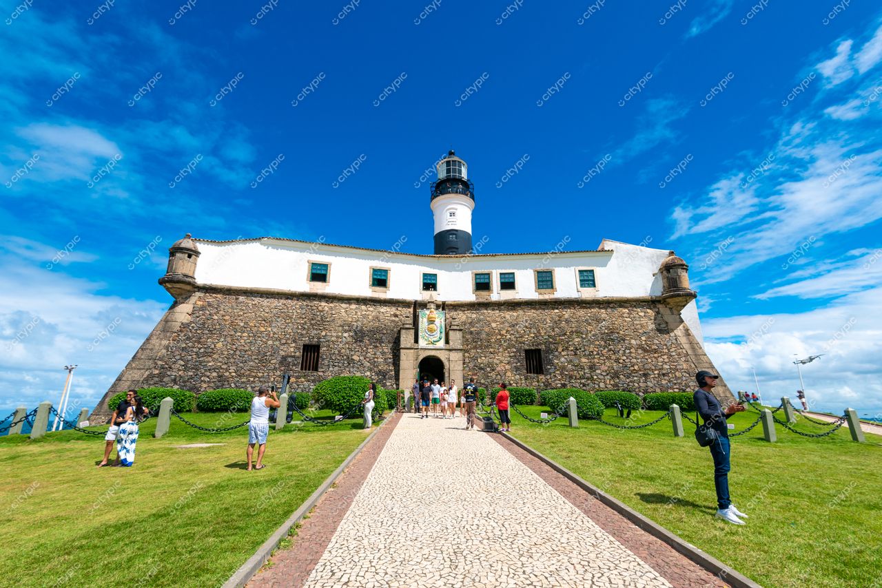 Salvador, Bahia, Farol da Barra em dia ensolarado com visitantes e vegetação ao redor, vista para o mar