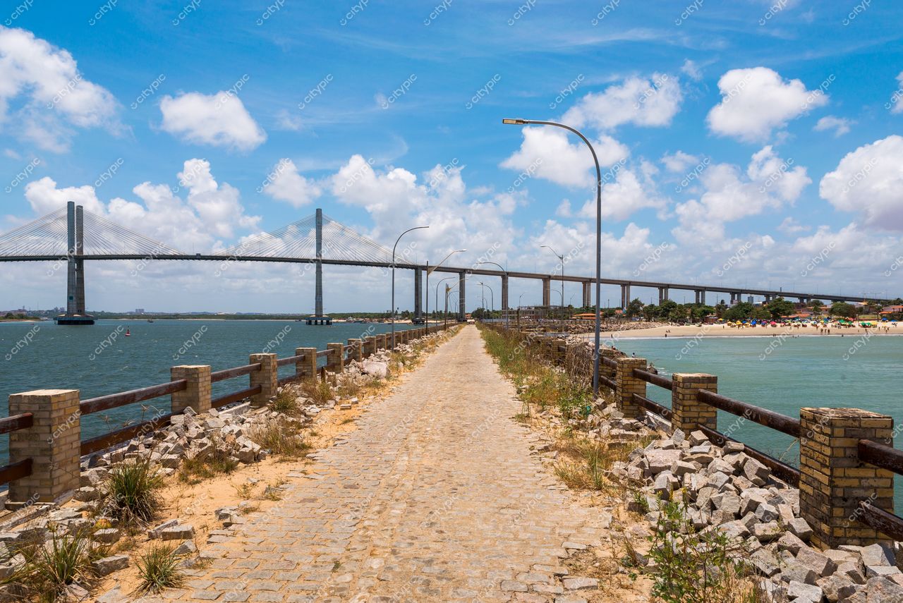 Natal, Rio Grande do Norte com calçadão iluminado e ponte ao fundo sob céu azul e nuvens brancas