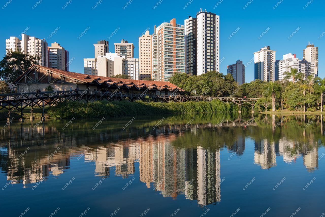 Curitiba, Paraná, vista diurna com edifícios modernos refletidos em lago e estrutura de madeira em primeiro plano