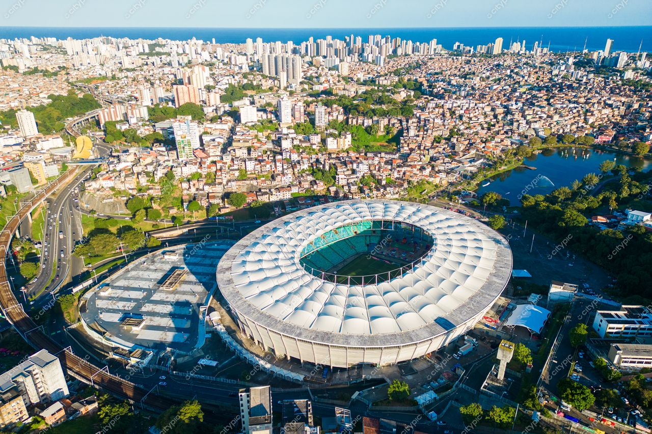 Salvador, Bahia vista aérea do Estádio Arena Fonte Nova com vegetação, tráfego leve e costa ao fundo em dia claro