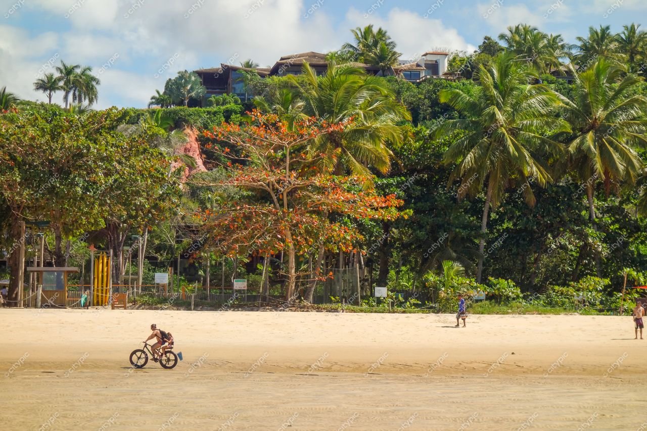 Arraial Dajuda, Bahia com praia iluminada pelo sol, vegetação densa e pessoas caminhando na areia