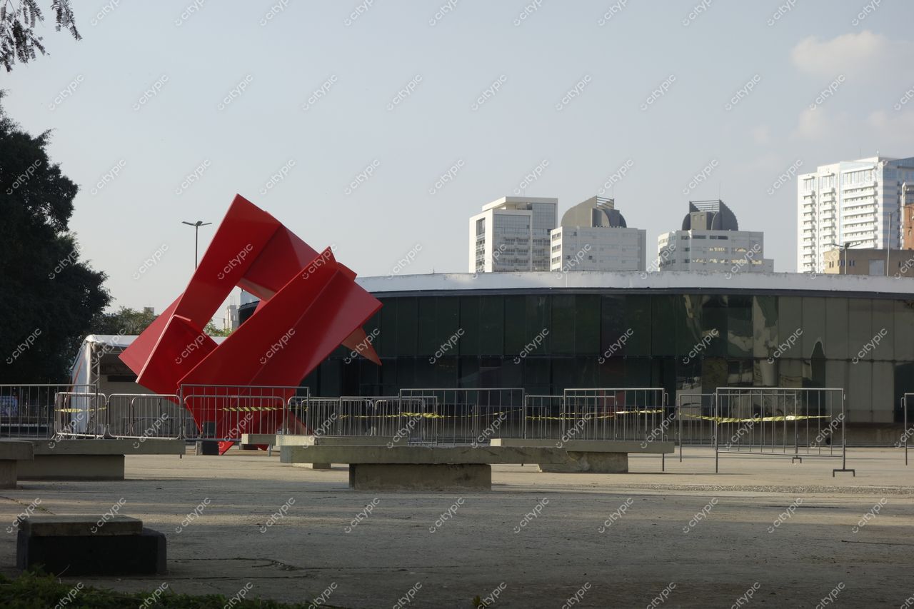 Parque Ibirapuera em São Paulo com escultura vermelha em destaque e edifícios modernos ao fundo sob luz suave