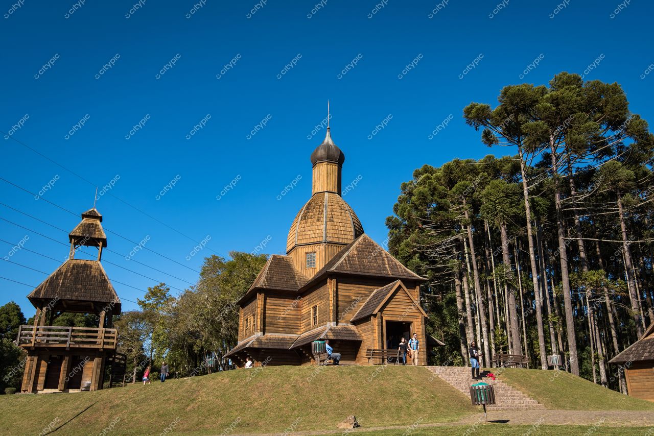 Curitiba, Paraná, construção rústica de madeira com telhado cônico em dia ensolarado e vegetação ao redor