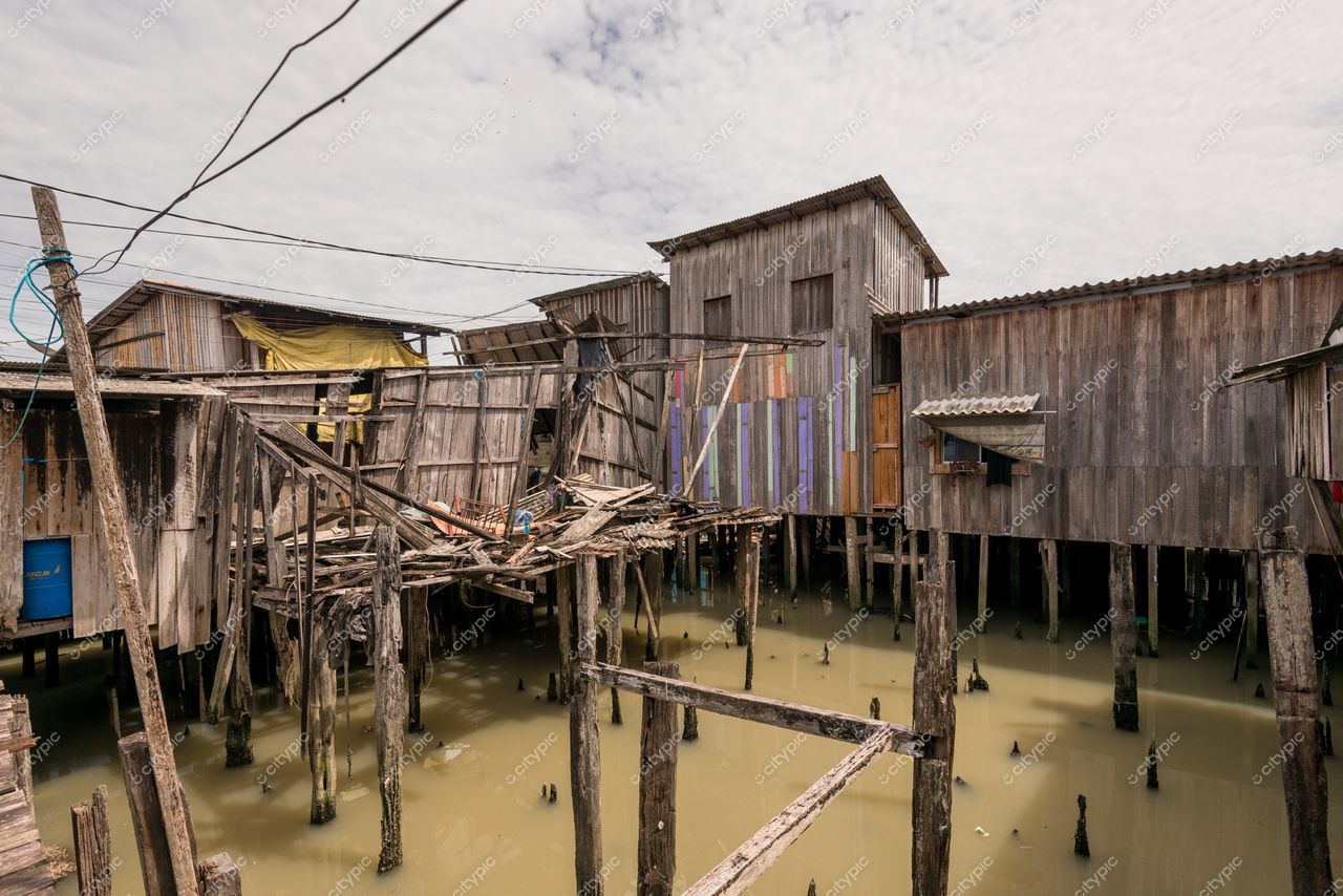 Belém, Pará retrata palafitas de madeira deterioradas sobre estacas com água turva e céu nublado ao fundo