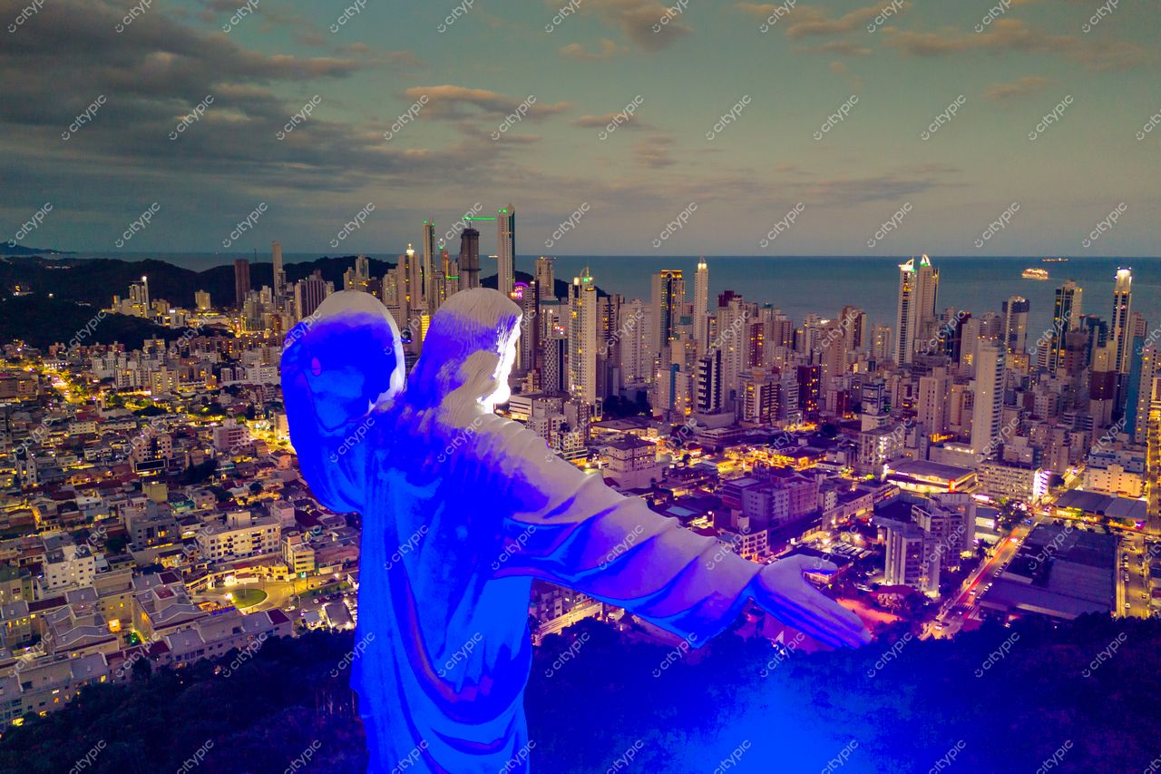Balneário Camboriú, Santa Catarina, Cristo Luz iluminado ao entardecer com edifícios altos e céu dramático