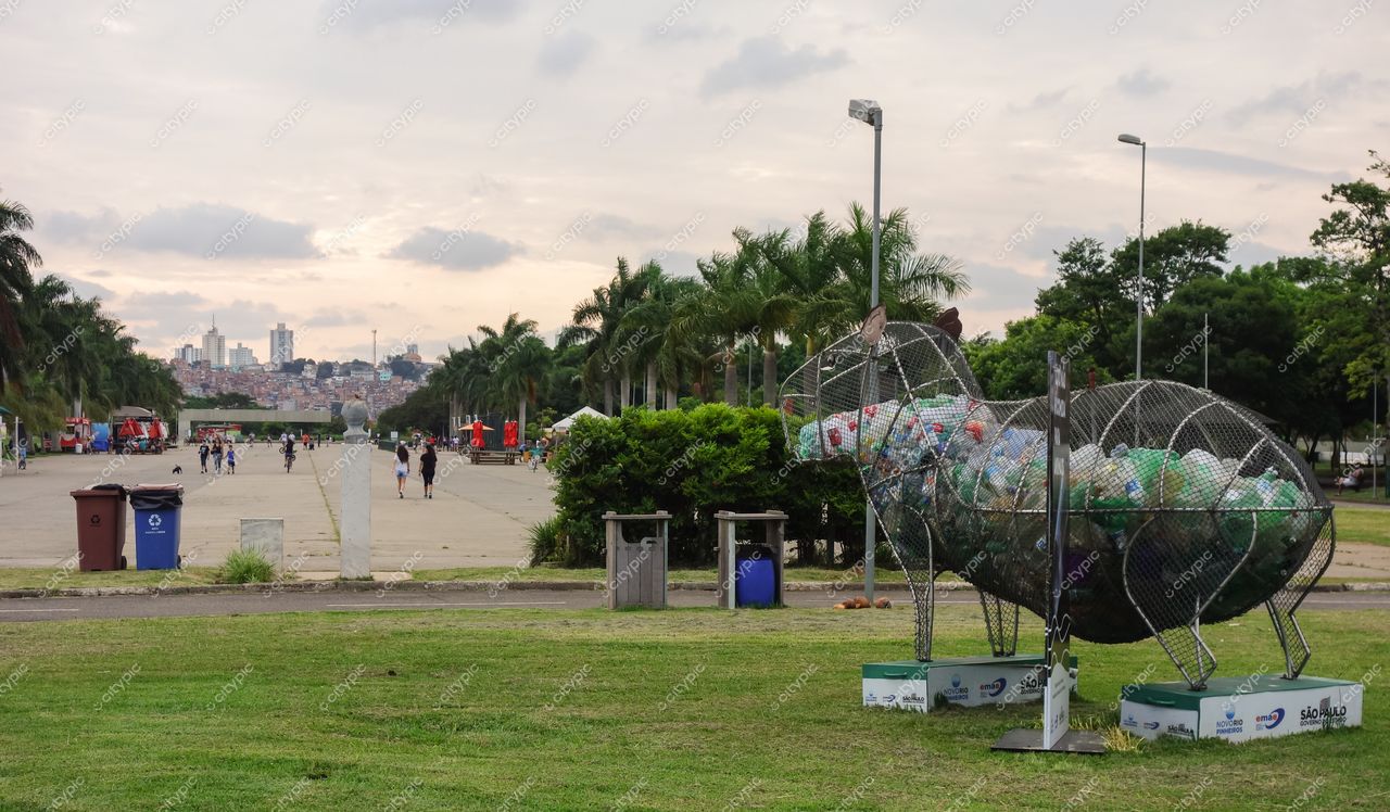 Parque Ibirapuera em São Paulo com escultura de animal em grade metálica e lixo reciclável ao entardecer