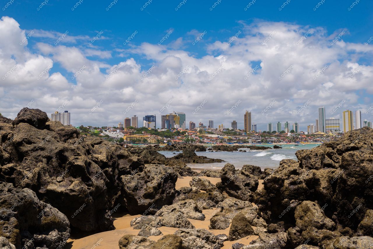 Natal, Rio Grande do Norte com rochas e areia em primeiro plano e arranha-céus ao fundo sob céu azul claro