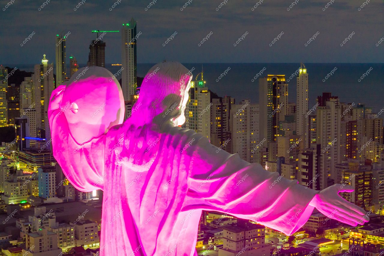Balneário Camboriú, Santa Catarina, escultura do Cristo Luz iluminada em rosa ao entardecer com edifícios modernos ao fundo