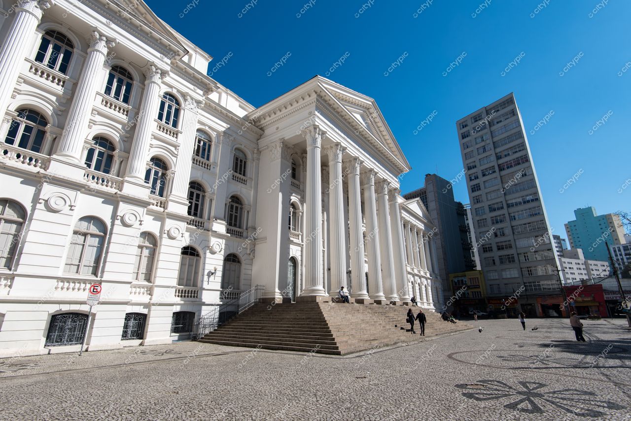Curitiba, Paraná, edifício histórico neoclássico com colunas brancas e escadarias em dia ensolarado com pessoas na praça