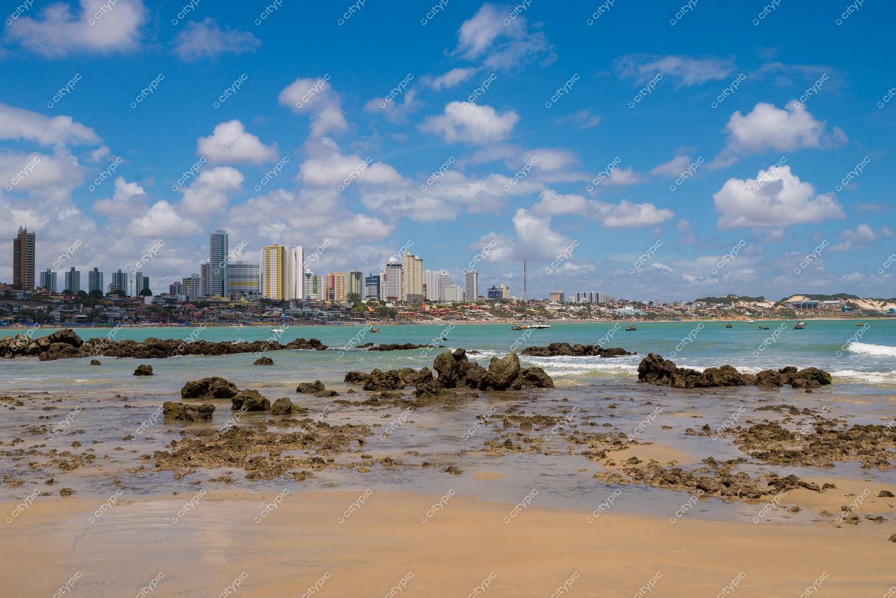Natal, Rio Grande do Norte com rochas na areia e edifícios urbanos sob céu azul em dia ensolarado