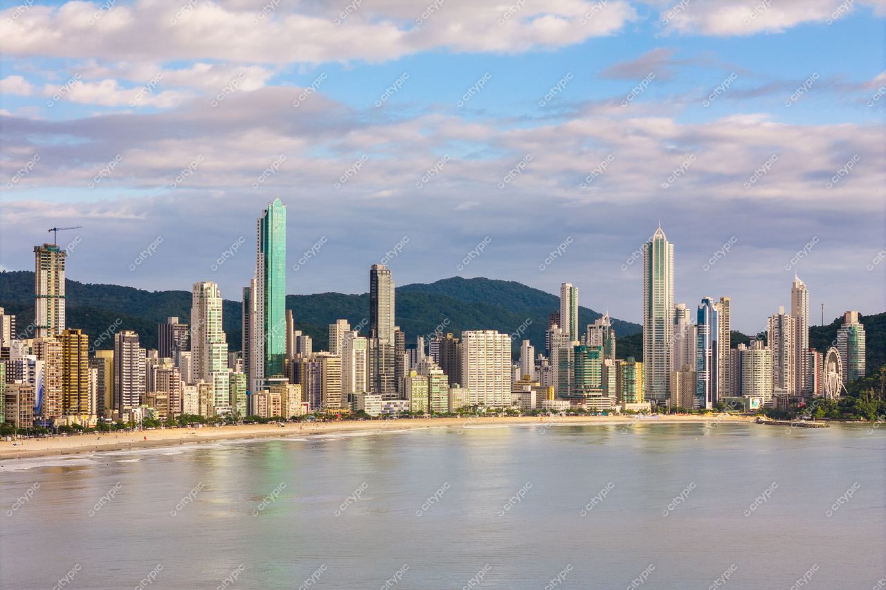 Balneário Camboriú, Santa Catarina, skyline com edifícios refletindo luz do sol e montanhas ao fundo em dia nublado