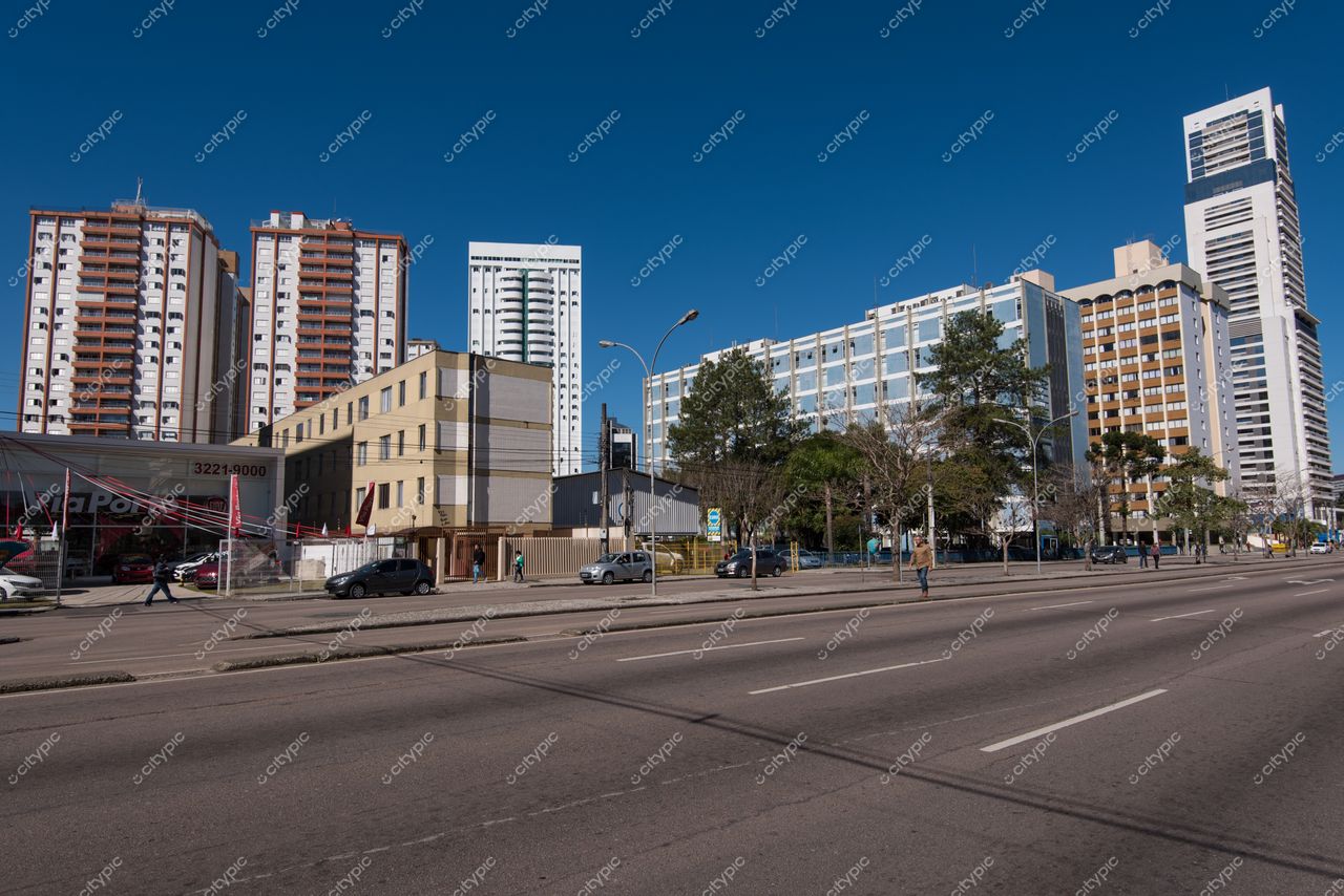 Curitiba, Paraná vista urbana com edifícios modernos e comerciais em dia ensolarado, veículos em movimento e vegetação