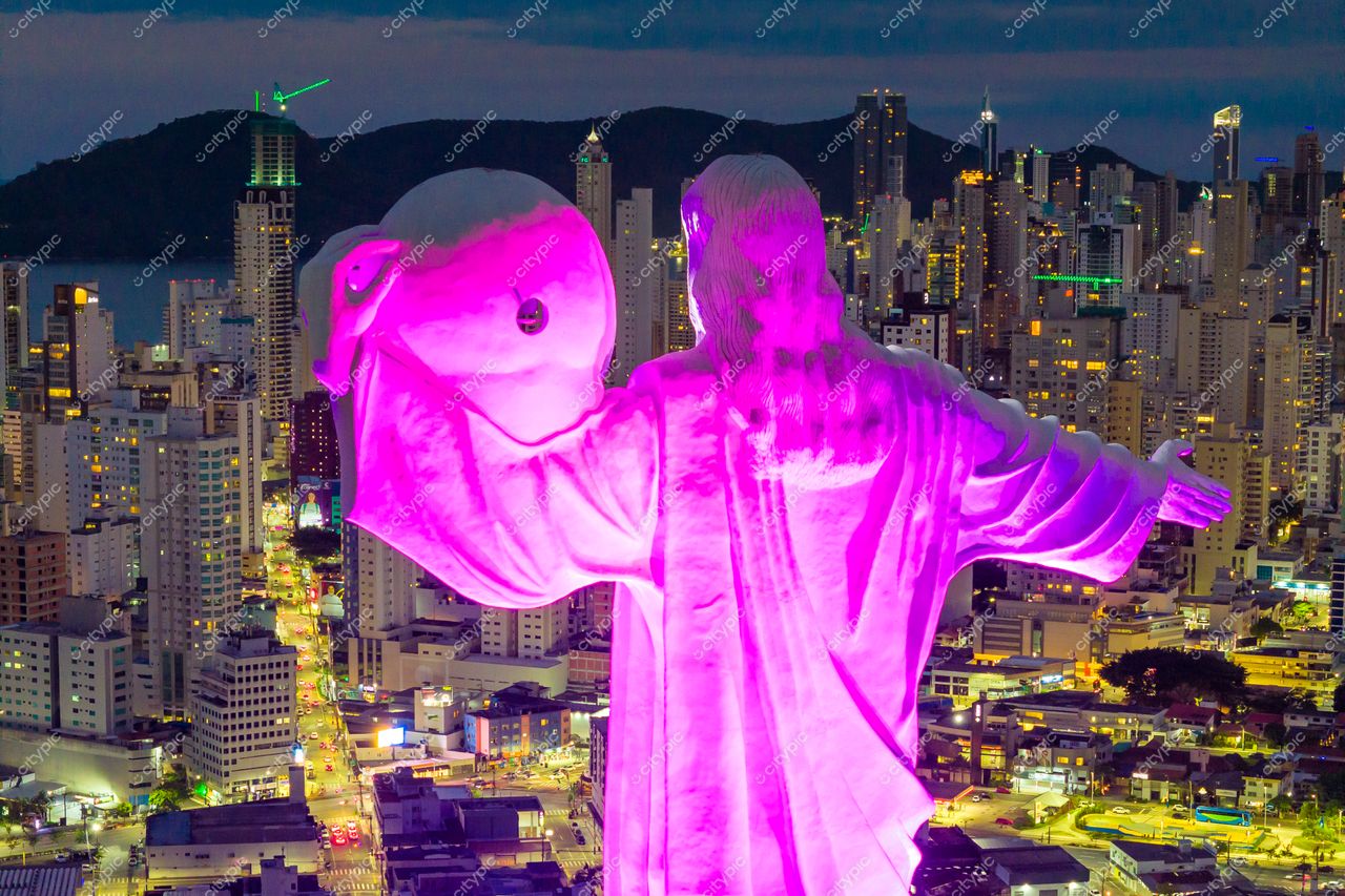 Balneário Camboriú, Santa Catarina, estátua do Cristo Luz iluminada em rosa ao entardecer com arranha-céus ao fundo
