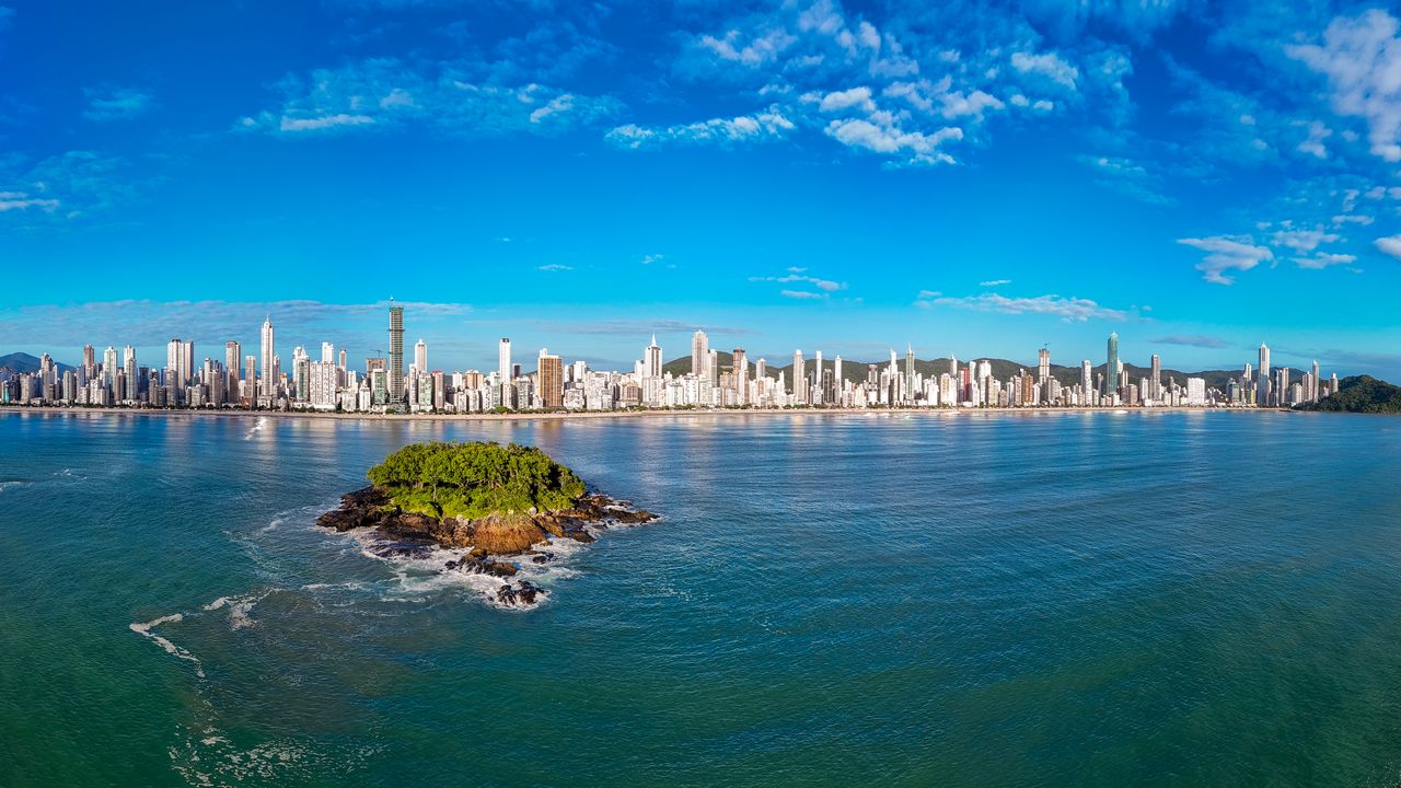 Balneário Camboriú, Santa Catarina vista panorâmica com edifícios altos, mar tranquilo e ilha verde em dia ensolarado