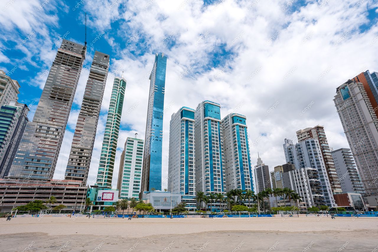 Balneário Camboriú, Santa Catarina, vista da praia com prédios altos de vidro sob céu claro e vegetação urbana