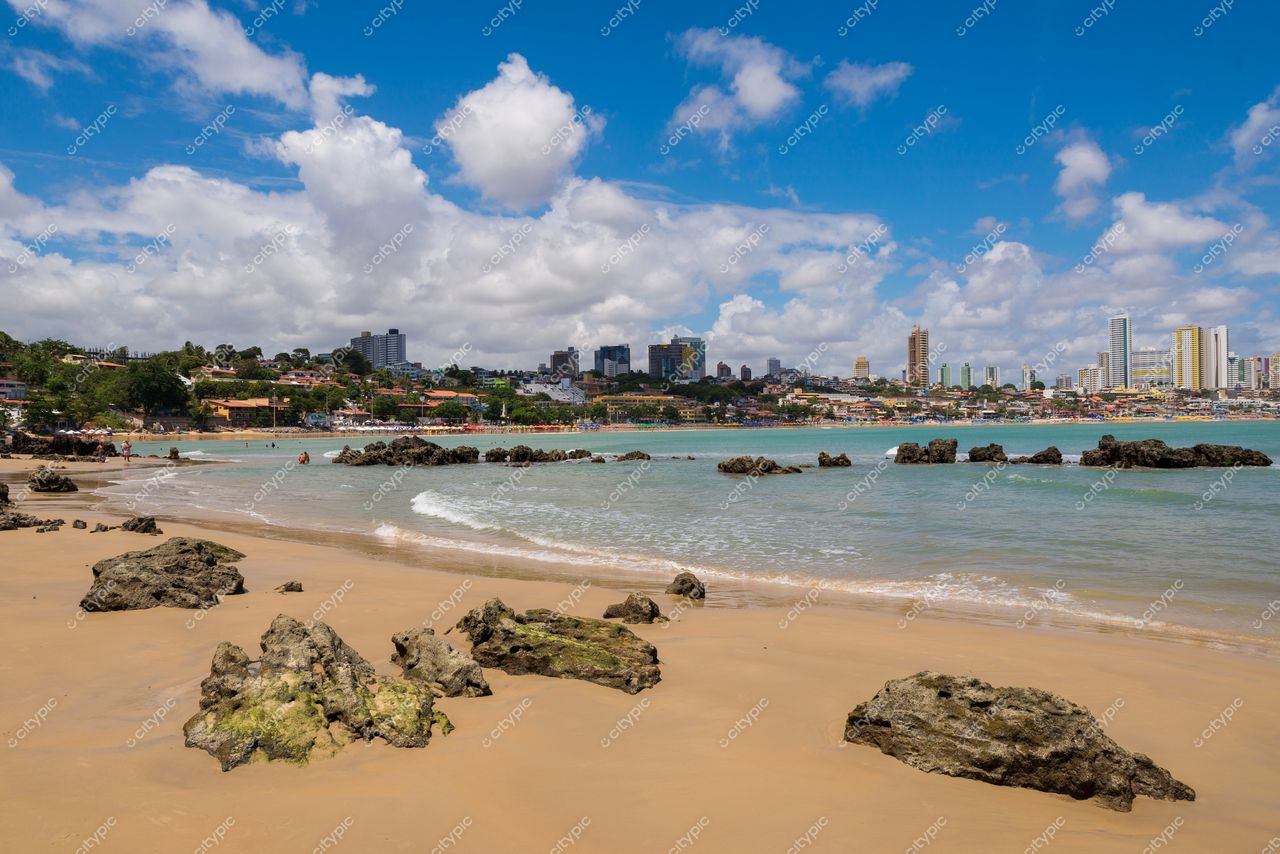 Natal, Rio Grande do Norte, praia com areias claras e mar calmo, prédios altos ao fundo sob céu nublado