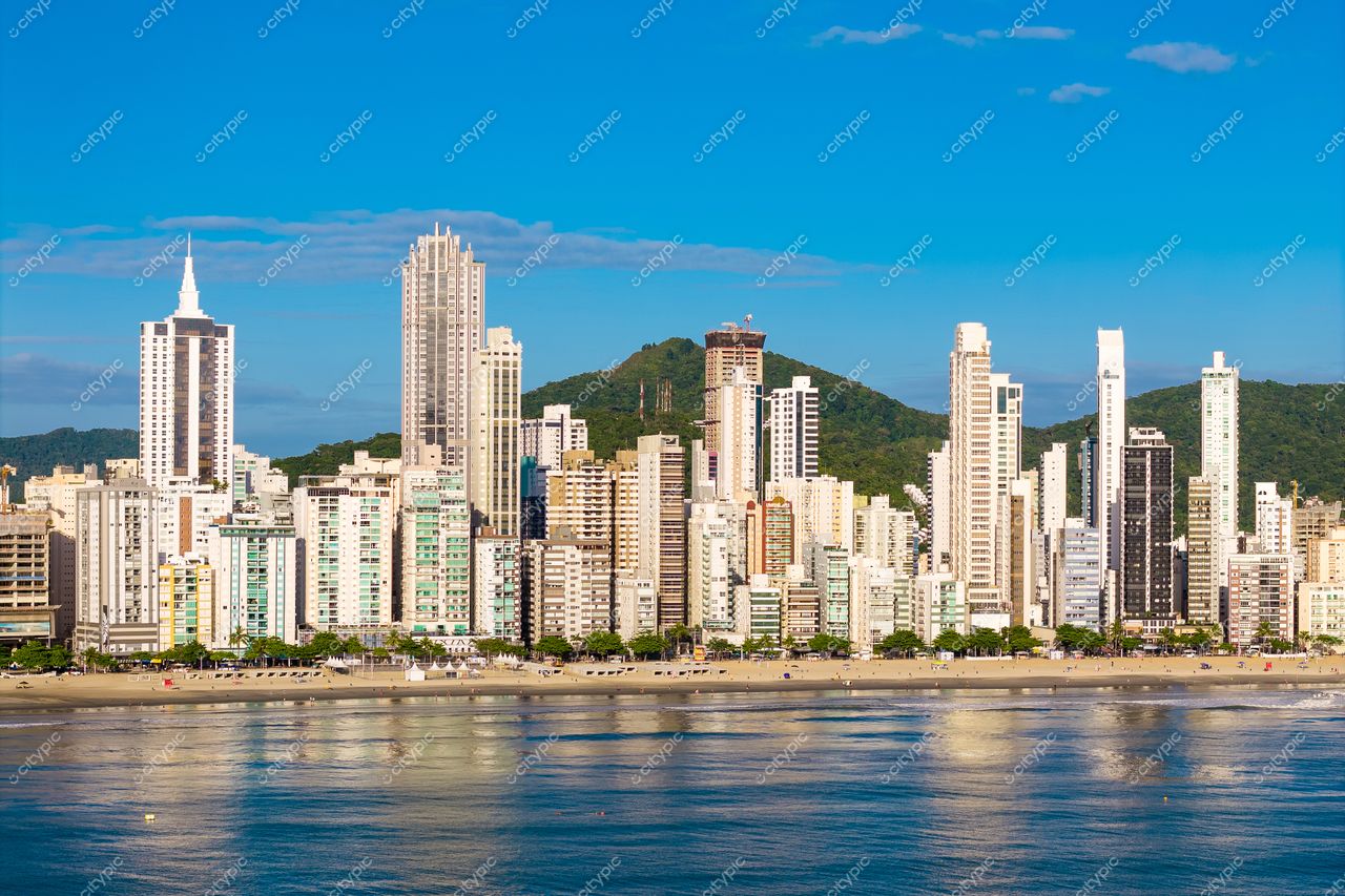 Balneário Camboriú, Santa Catarina, orla com arranha-céus modernos refletindo na água em dia ensolarado e colinas verdes