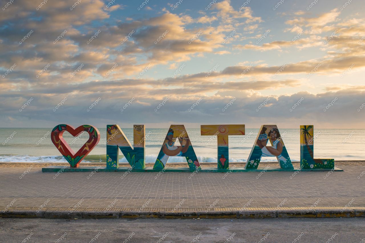 Natal, Rio Grande do Norte, estrutura artística “I ♥ NATAL” à beira-mar com céu nublado e luz suave do amanhecer