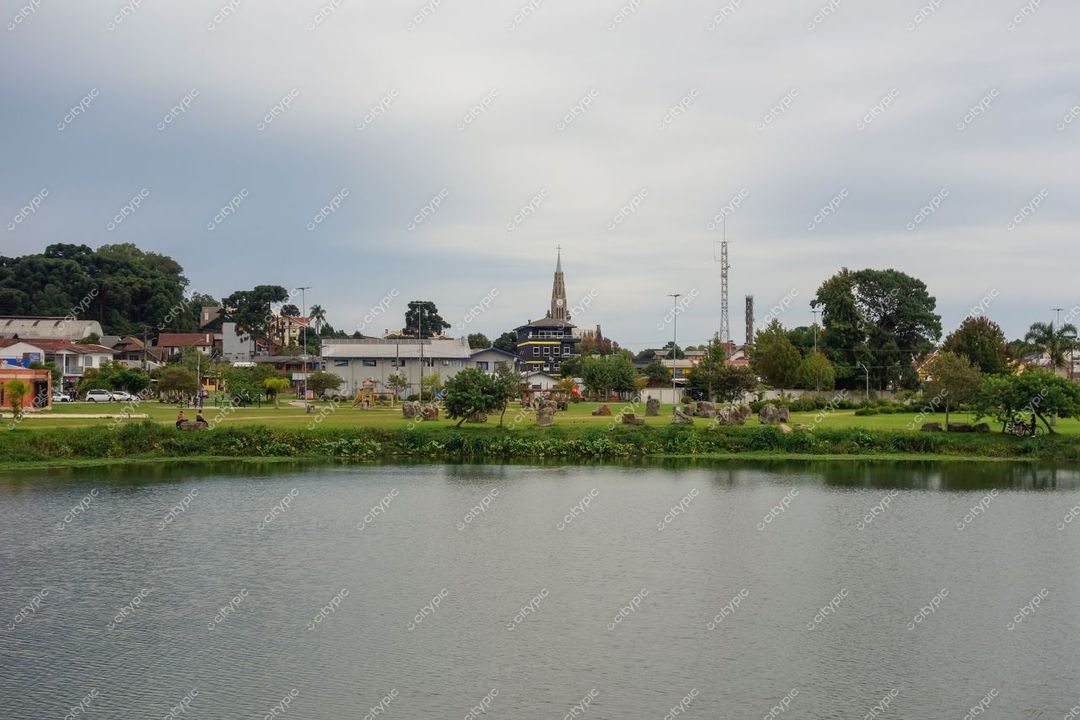 Canela, Rio Grande do Sul com lago tranquilo em primeiro plano e igreja de torre alta sob céu nublado