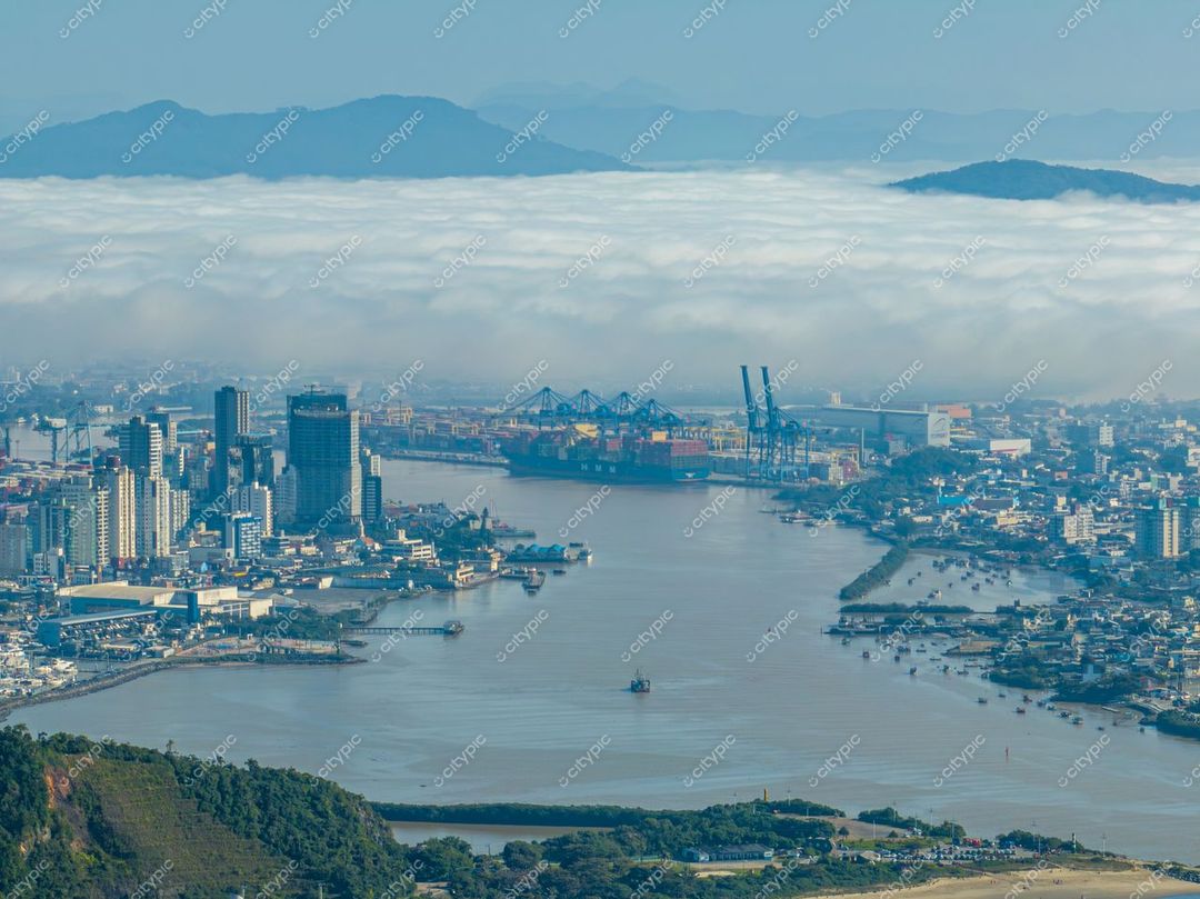 Itajaí, Santa Catarina vista aérea com infraestrutura portuária, rio serpenteando e montanhas ao fundo em luz suave