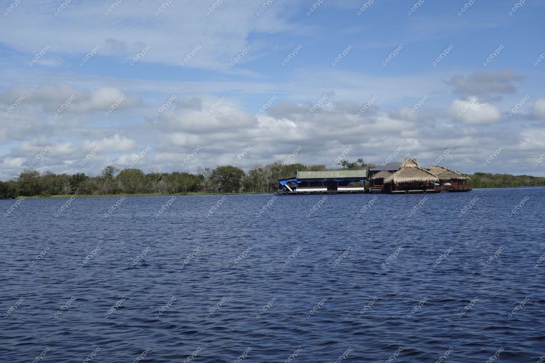 Manaus, Amazonas, vista tranquila do rio com reflexos, construções de palha e moderna, vegetação densa ao fundo