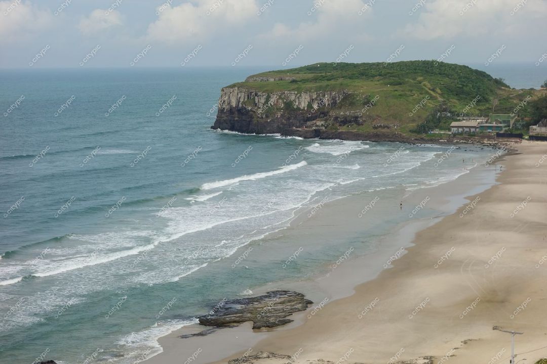 Torres, Rio Grande do Sul, praia tranquila com areia clara, penhasco verdejante e céu parcialmente nublado
