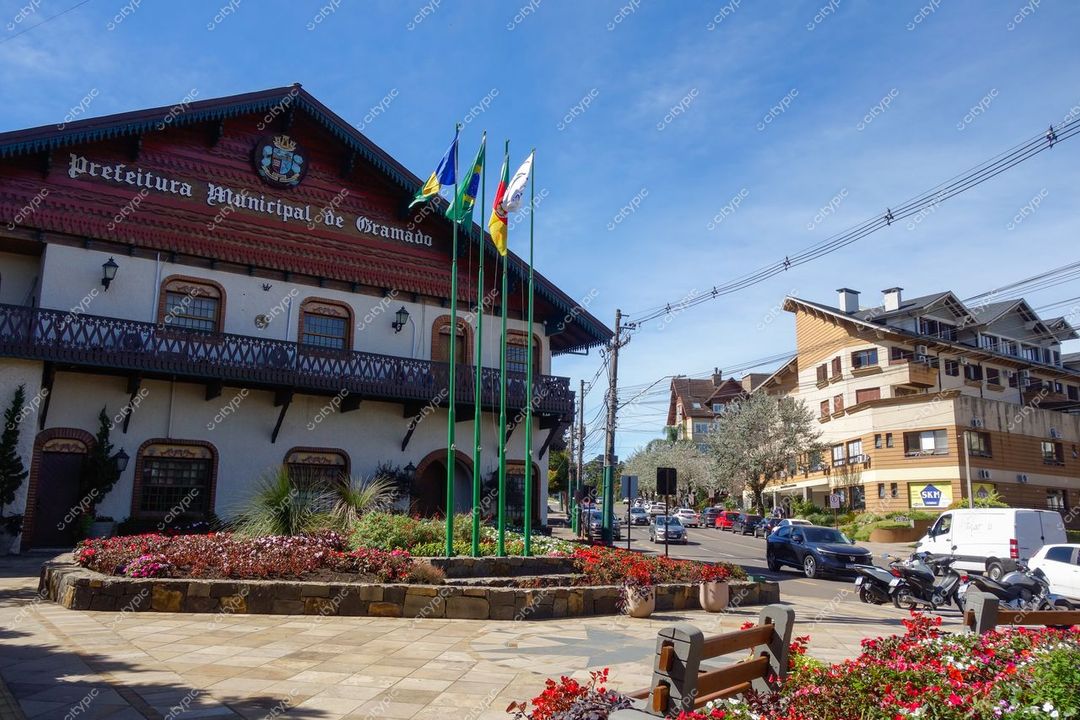 Gramado, Rio Grande do Sul, Prefeitura Municipal com bandeiras e canteiros floridos em dia ensolarado e tráfego urbano