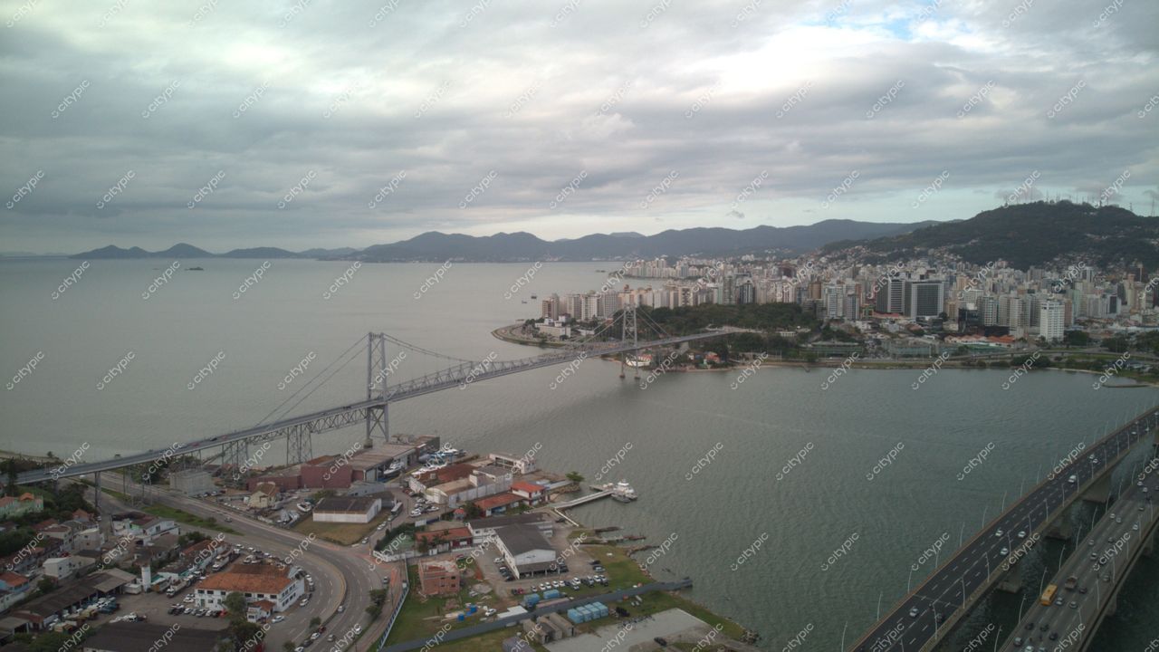 Centro de Florianópolis com vista da ponte, mar calmo, céu nublado e tráfego moderado nas ruas urbanas