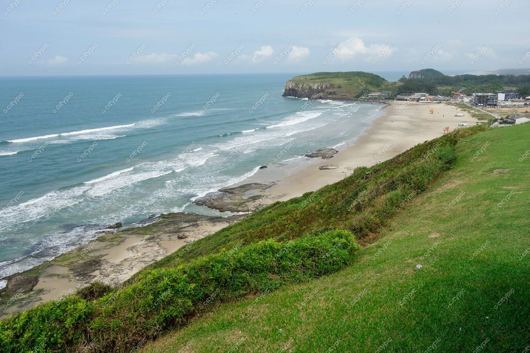 Torres, Rio Grande do Sul, vista panorâmica da praia com penhasco, vegetação verde e céu parcialmente nublado