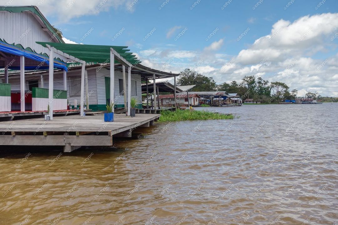 Manaus, Amazonas, casas em palafitas à beira de rio com vegetação amazônica e céu parcialmente nublado durante o dia