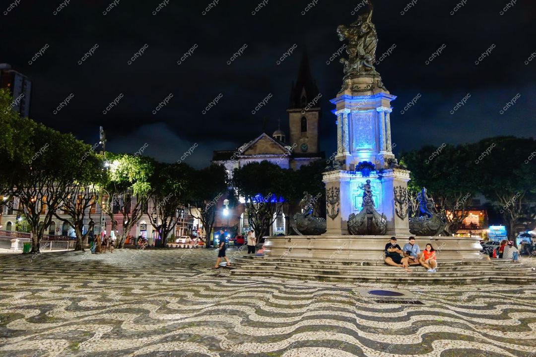 Manaus, Amazonas, Praça de São Sebastião à noite com monumento iluminado em azul e árvores podadas ao redor