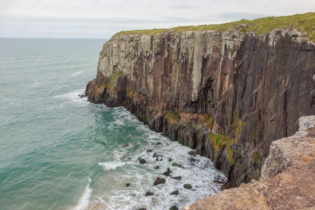Torres, Rio Grande do Sul, precipício com rochas verticais e vegetação rasteira sob céu nublado e mar azul claro