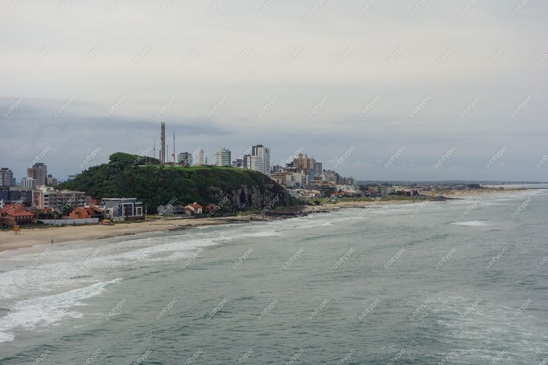 Torres, Rio Grande do Sul, praia com ondas suaves e colina verdejante sob céu nublado ao amanhecer