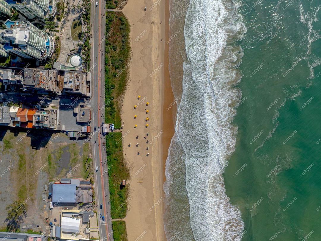 Itajaí, Santa Catarina vista aérea com costa de areia clara, edifícios à orla e guarda-sóis amarelos na praia